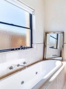 La salle de bains est pourvue d'une baignoire blanche et d'une fenêtre. dans l'établissement Spacious, light-filled retreat, à Warrnambool