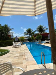 une piscine avec des chaises et un parasol dans l'établissement Condomínio Arituba Tropical, à Nísia Floresta