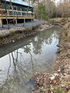 a river with a house in the background next to a house at Livin on the Edge Cabin in Albert Pike, Brand New! in Caddo Gap