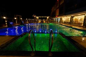 una piscina por la noche con iluminación azul y verde en Royal Palace Beach Resort en Mandarmoni