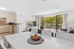 Santa Monica Apartments - Hosted by Burleigh Letting في غولد كوست: مطبخ وغرفة معيشة مع طاولة بيضاء مع وعاء من الفواكه