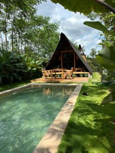 a thatch roofed hut with a pool of water at Villa Verde the garden in Kejayan