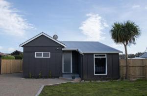 a black house with a palm tree in a yard at The Flight Pad Aisle Seat Pet Friendly in Waitara
