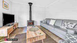 ein Wohnzimmer mit einer Couch, einem Tisch und einem Fernseher in der Unterkunft Horseshoe Beach House 4 Young Street, Bermagui in Bermagui