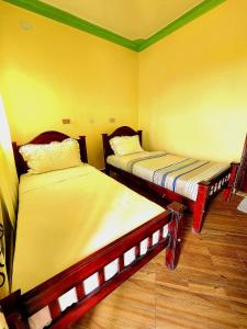 2 Betten in einem Zimmer mit gelben Wänden und Holzböden in der Unterkunft Lights of kazinga orphanage and homestay in Rubirizi