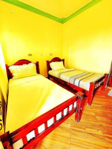 two beds in a room with yellow walls and wooden floors at Lights of kazinga orphanage and homestay in Rubirizi