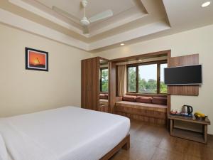 a bedroom with a bed and a couch and a television at Pride Biznotel Sasan Gir in Sasan Gir