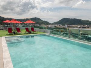 einen Pool auf einem Gebäude mit Stühlen und Sonnenschirmen in der Unterkunft Neon Patong in Patong Beach