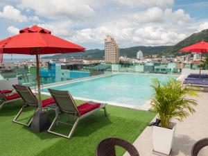 einen Pool mit 2 Stühlen und einem roten Regenschirm in der Unterkunft Neon Patong in Patong Beach