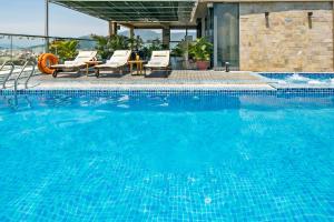 a large blue swimming pool with chairs and a table at Bliss Luxury Hotel in Da Nang