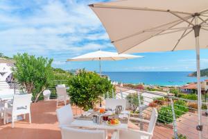 a patio with a table and an umbrella and the ocean at Hotel Punta Est in Baja Sardinia