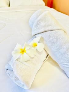 a white towel with two white flowers on a bed at Suriyan Villa Erawan Kanchanaburi สุริยัน วิลล่า เอราวัณ กาญจนบุรี in Tha Kradan