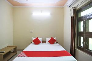 OYO 62761 Hotel Daksh في Mahendragarh: غرفة نوم بسرير ومخدات حمراء ونافذة