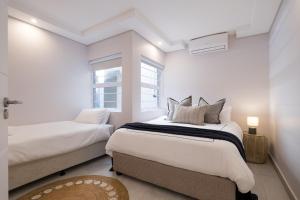 a white bedroom with two beds and a window at The Blonde Bungalow Ballito in Ballito