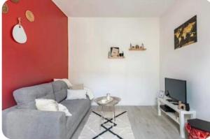 a living room with a gray couch and a red wall at Maison cosy Paris Orly jardin privée in Vitry-sur-Seine