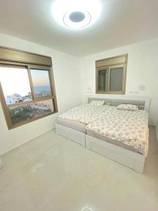 um quarto branco com uma cama e 2 janelas em the pool on the sea em Netanya