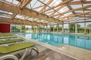 a large swimming pool with green chairs in a building at Pierre & Vacances Résidence Le Chant des Oiseaux in Courseulles-sur-Mer