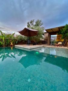 a swimming pool with an umbrella next to a house at Le Figuier du Lac Bin elouidane in Bine el Ouidane