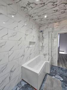 La salle de bains est pourvue d'une baignoire blanche et de murs en marbre. dans l'établissement LUXE Villa Near NEC, BHX & Train, à Birmingham