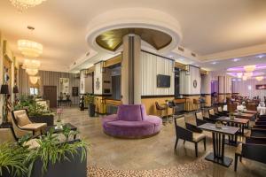 um átrio de hotel com um sofá roxo, mesas e cadeiras em Grand Hotel Glorius Makó em Makó