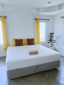 a large white bed in a white room with yellow curtains at Thongtalay Bed & Breakfast Koh Larn in Ko Larn