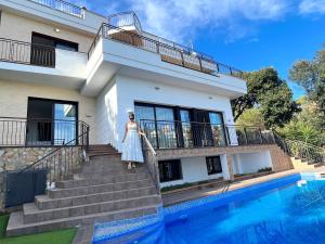 una mujer parada en las escaleras de una casa al lado de una piscina en Villa de lujo con vistas al mar y piscina privada, en Santa Susanna