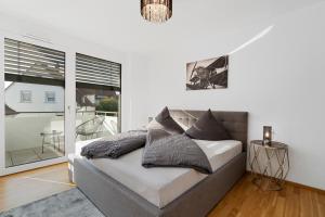 a white bedroom with a bed and a balcony at ANYTIME - Riedlepark Apartments in Friedrichshafen