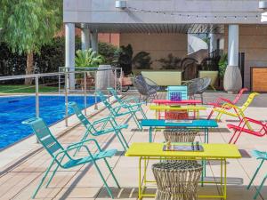 - un groupe de tables et de chaises colorées à côté d'une piscine dans l'établissement Novotel Barcelona Cornellà, à Cornellà de Llobregat