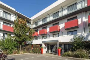 um edifício de apartamentos com varandas vermelhas e um parque de estacionamento em Best Western Les Aureliades Saint Nazaire em Trignac