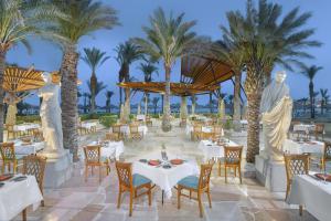 un restaurante con palmeras, mesas y sillas blancas en Jaz Fayrouz, en Sharm El Sheikh