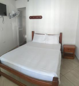 a bedroom with a bed with white sheets and a television at Hotel Zarina in Villavicencio