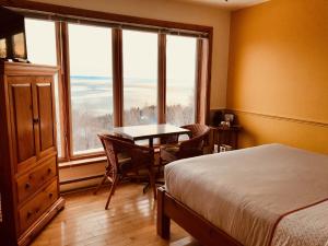 Schlafzimmer mit einem Bett, einem Tisch und Fenstern in der Unterkunft Auberge Cap aux Corbeaux in Baie-Saint-Paul
