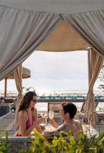 two people sitting at a table with glasses of wine at Kardia Resort Gili Trawangan A Pramana Experience in Gili Trawangan