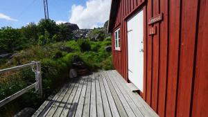 a red building with a white door and a wooden walkway at Real fisherman's cabins in Ballstad, Lofoten - nr. 11, Johnbua in Ballstad