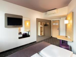 a hotel room with a bed and a desk and a tv at B&B HOTEL Düsseldorf-Mitte in Düsseldorf