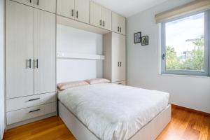 a white bedroom with a bed and a window at Athena's South Apartment in Athens