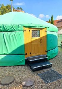 a green and yellow tent with a door and steps at Jurte 