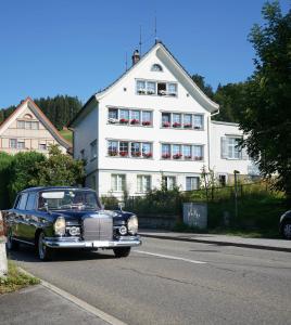 une vieille voiture garée devant un bâtiment blanc dans l'établissement Bergnestli, à Oberegg