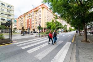two people walking across a crosswalk on a city street at Apartamento Palacio céntrico y silencioso 4-8 personas in Granada