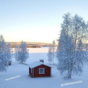 una pequeña cabaña roja en la nieve junto a un lago en Villa Haaveranta - Cosy cabin by the lake, en Rovaniemi