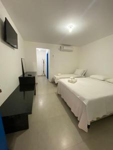 a white bedroom with two beds and a television at Suite Grega 5- Centro da Vila Abrãao in Abraão