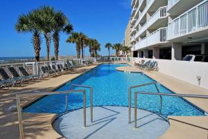 a swimming pool with chairs and palm trees and a building at Crescent Shores South - 510 in Myrtle Beach