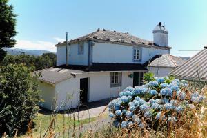 uma casa branca com flores azuis em frente em The Cliffs - Picon Seaside Cottage em Loiba