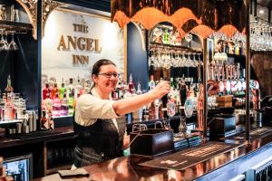 a woman standing behind a bar making a drink at The Angel Inn - The Inn Collection Group in Bowness-on-Windermere