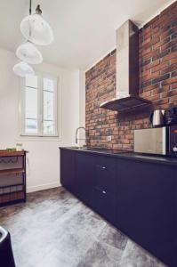 a kitchen with black cabinets and a brick wall at Studio Cosy Tout Confort Porte Orléans 2 Pers Paris in Montrouge