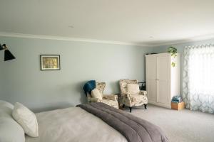 a bedroom with a bed and two chairs and a cabinet at Birdsong Cottage in Paraparaumu