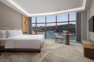 Crowne Plaza Zhoushan Seaview, an IHG Hotel في زهوشان: غرفة فندقية بسرير ونافذة كبيرة