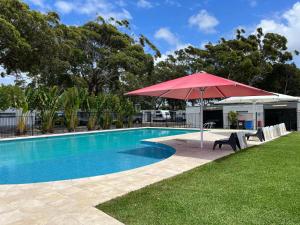a swimming pool with a red umbrella and a table and chairs at Shelly Beach Holiday Park in The Entrance