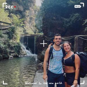 a man and a woman standing in front of a waterfall at Wally House青山惠风民宿 in Zhangjiajie