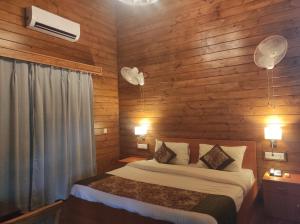 a bedroom with wooden walls and a bed with two lamps at Jironi Resort in Charduār